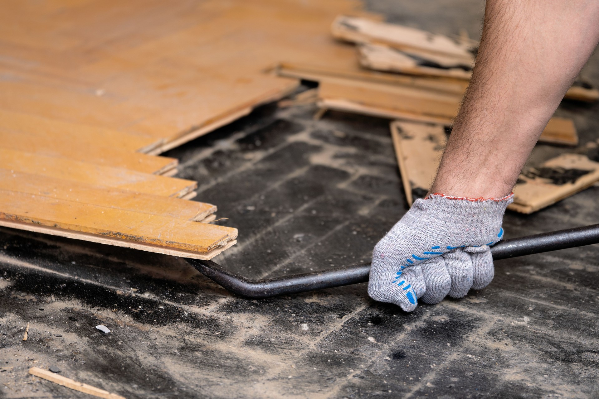 Worker removes old flooring using a tire iron tool